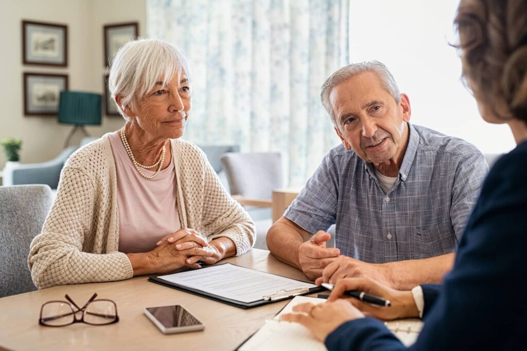 Two seniors sitting at a table with a woman with a clipboard in front of them