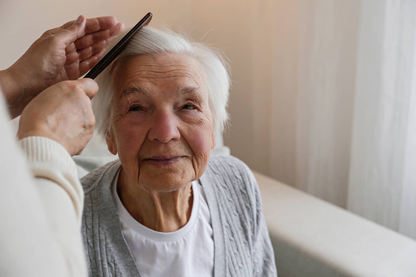 An elderly woman is getting her hair combed