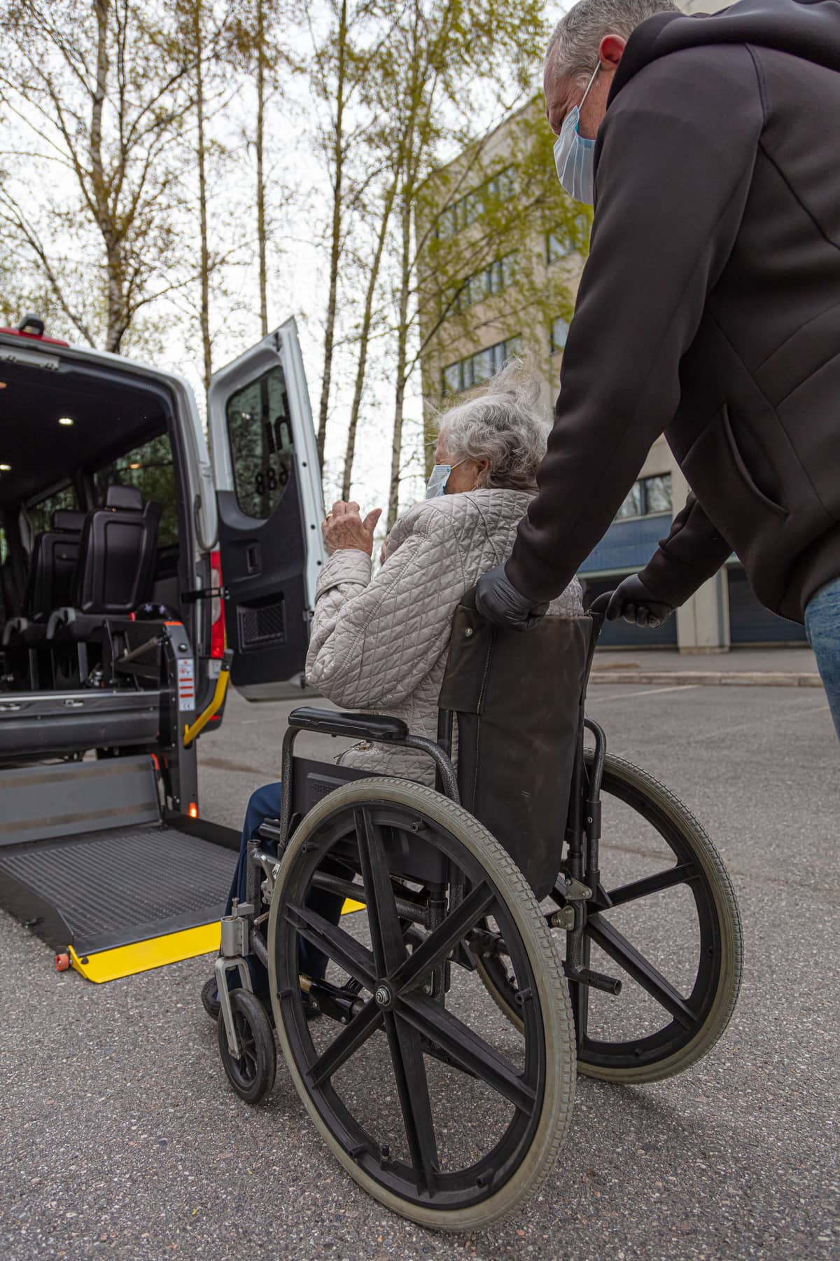 A man using a wheelchair lift to get a woman in a wheelchair into a van