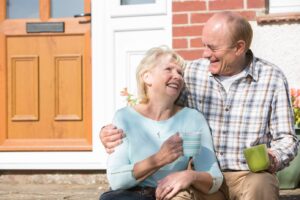 An elderly couple sitting on the steps outside their home drinking coffee