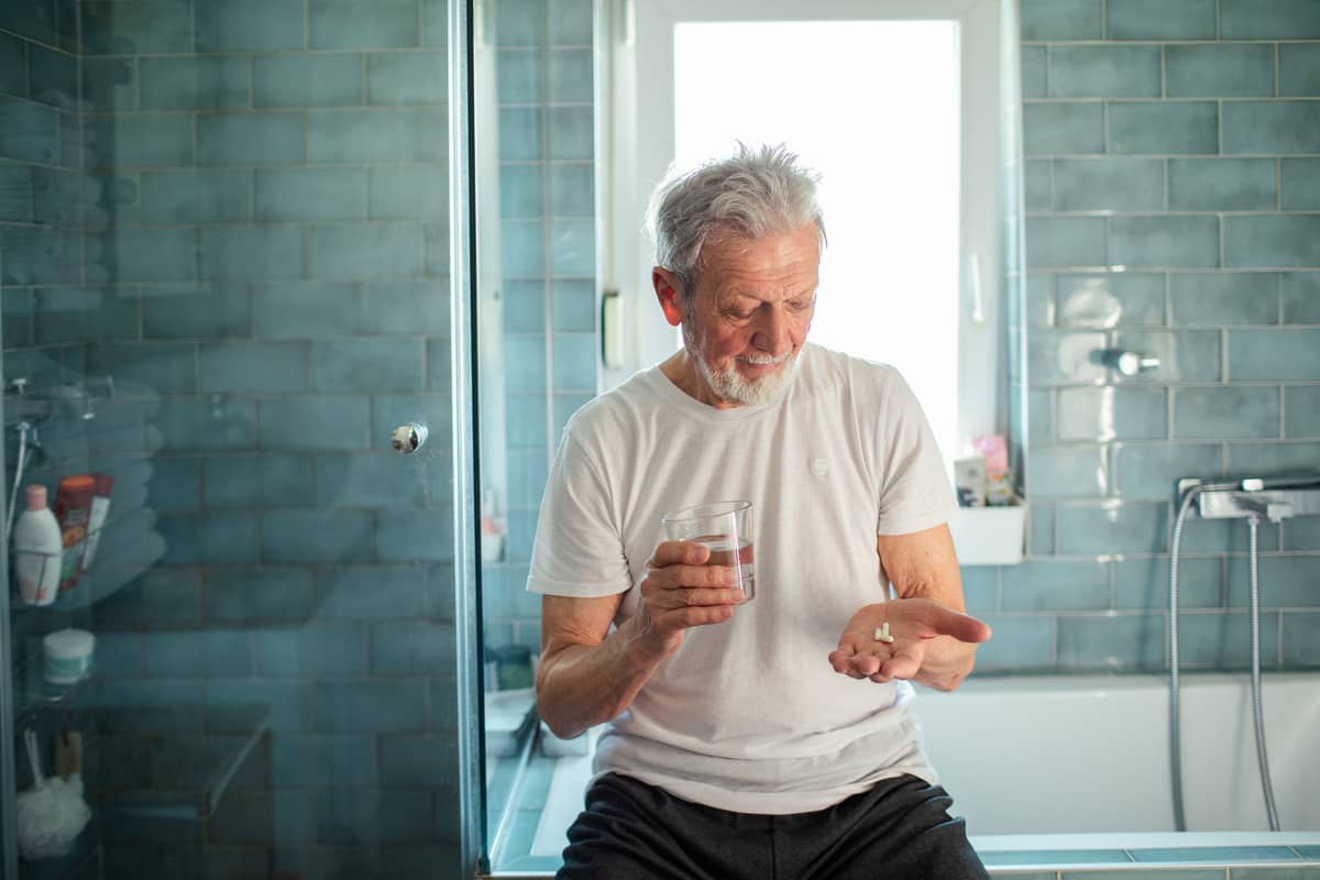 A senior man sitting in the bathroom taking his medicine