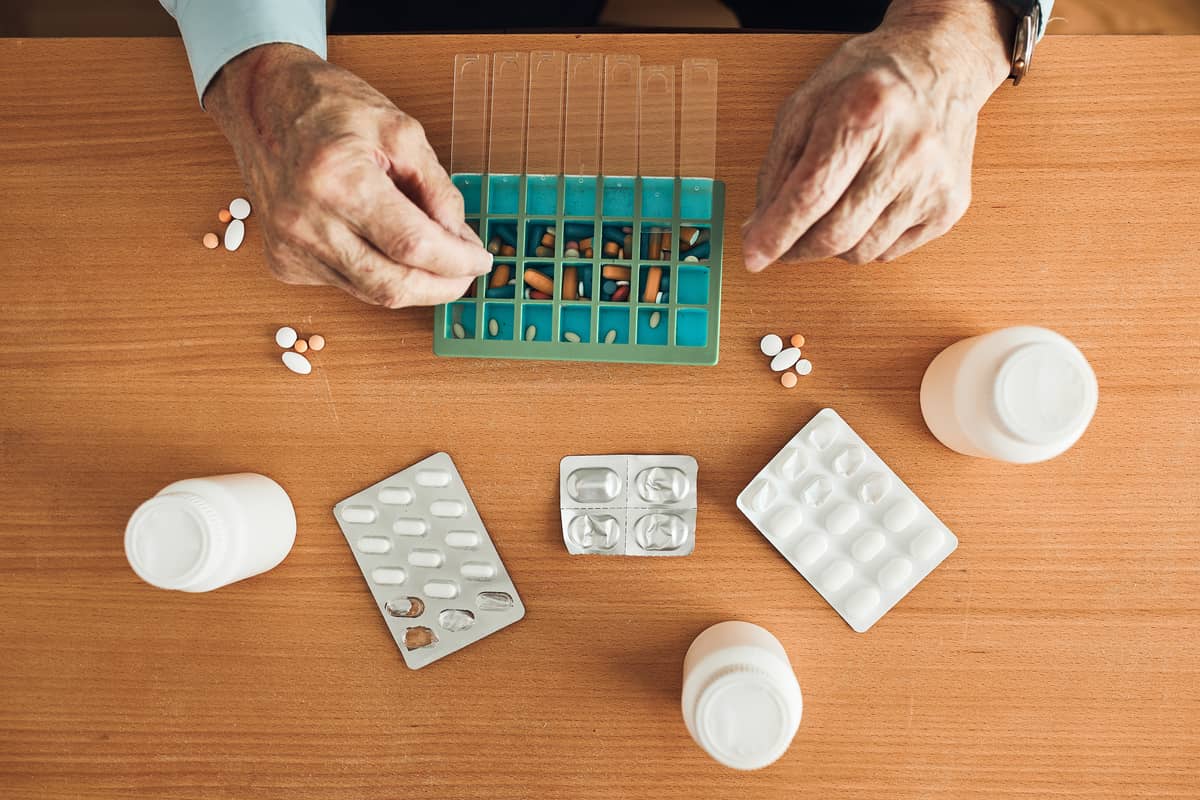 The hands of an elderly man putting his medicine in a pill box