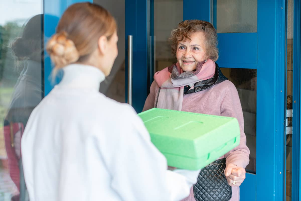 Someone bringing a senior woman a meal to her door (example of Meals on Wheels)