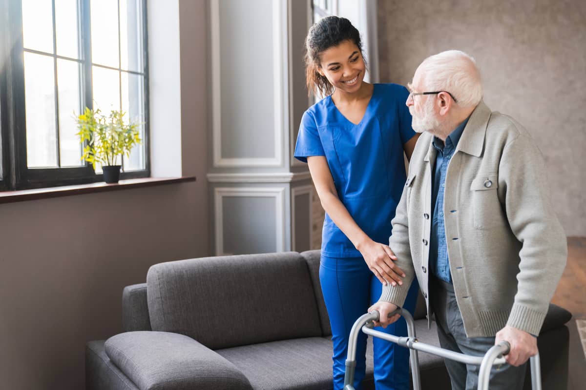 A caregiver helping a senior man move around the house
