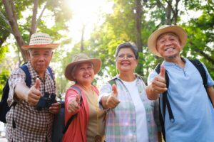 A group of seniors that look like they have been hiking smiling at the camera and giving a thumbs up