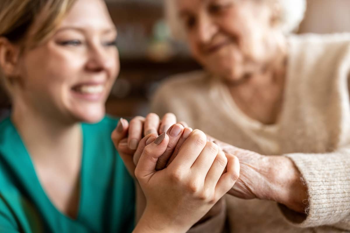 A caregiver talking to and holding hands with a senior woman