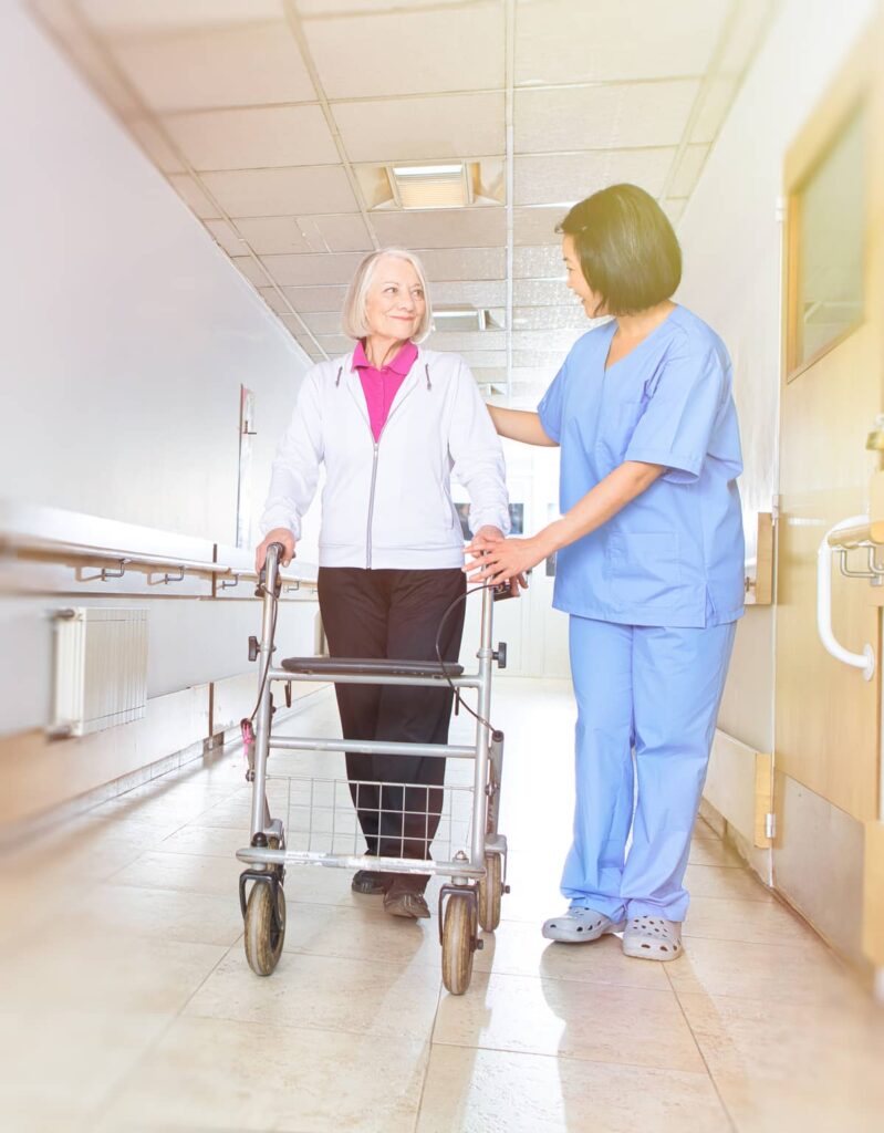 A nurse walking with a senior woman (who is using a walker) in the hospital hallway