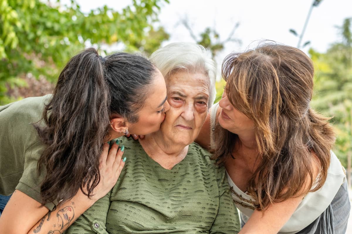 Two women (probably daughters) kissing a senior woman's cheeks
