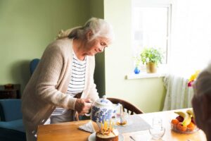 A senior woman in her home pouring tea with a birthday cake on a table