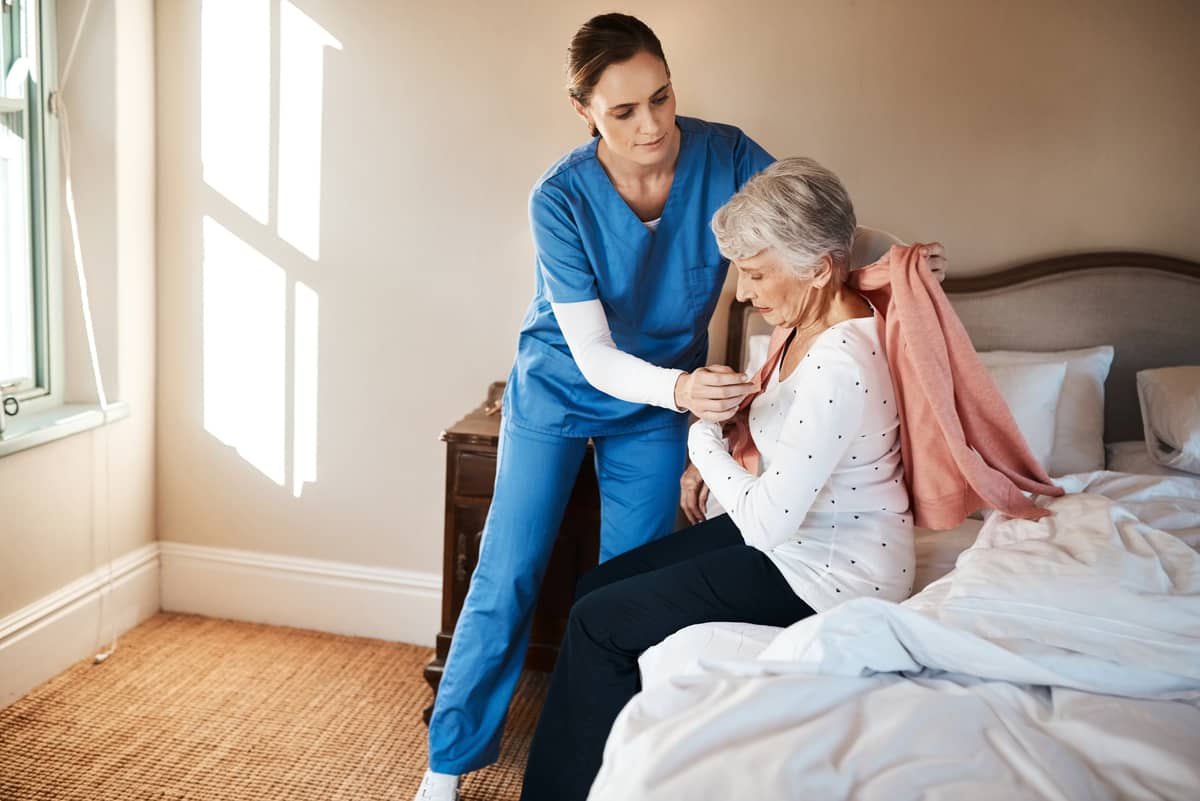 A caregiver helping a senior woman put on a sweater
