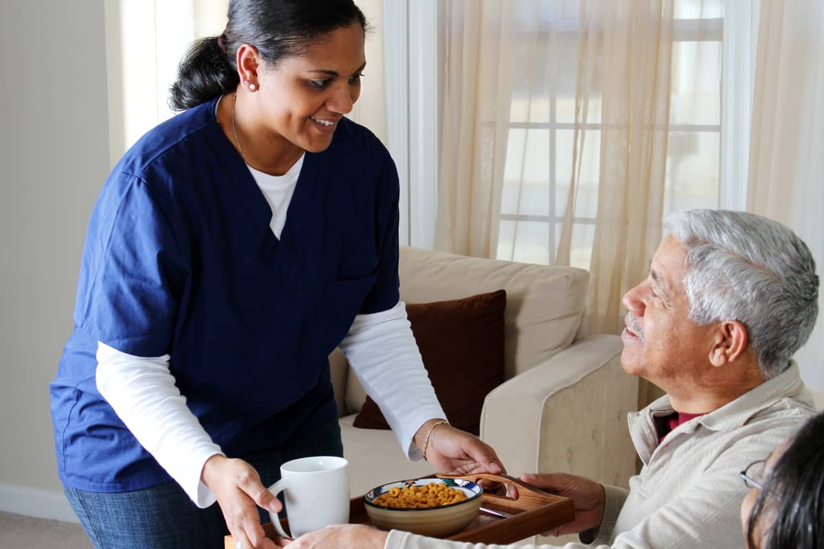 A caregiver is bring a senior man breakfast in his home