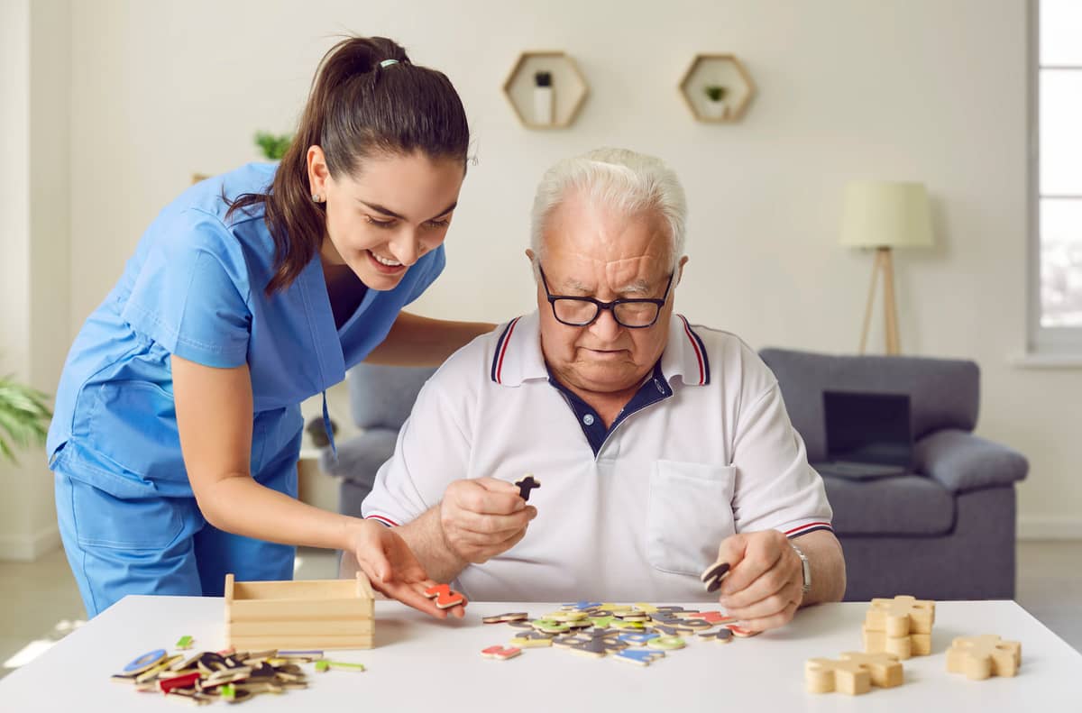 A caregiver is helping a senior man with a puzzle