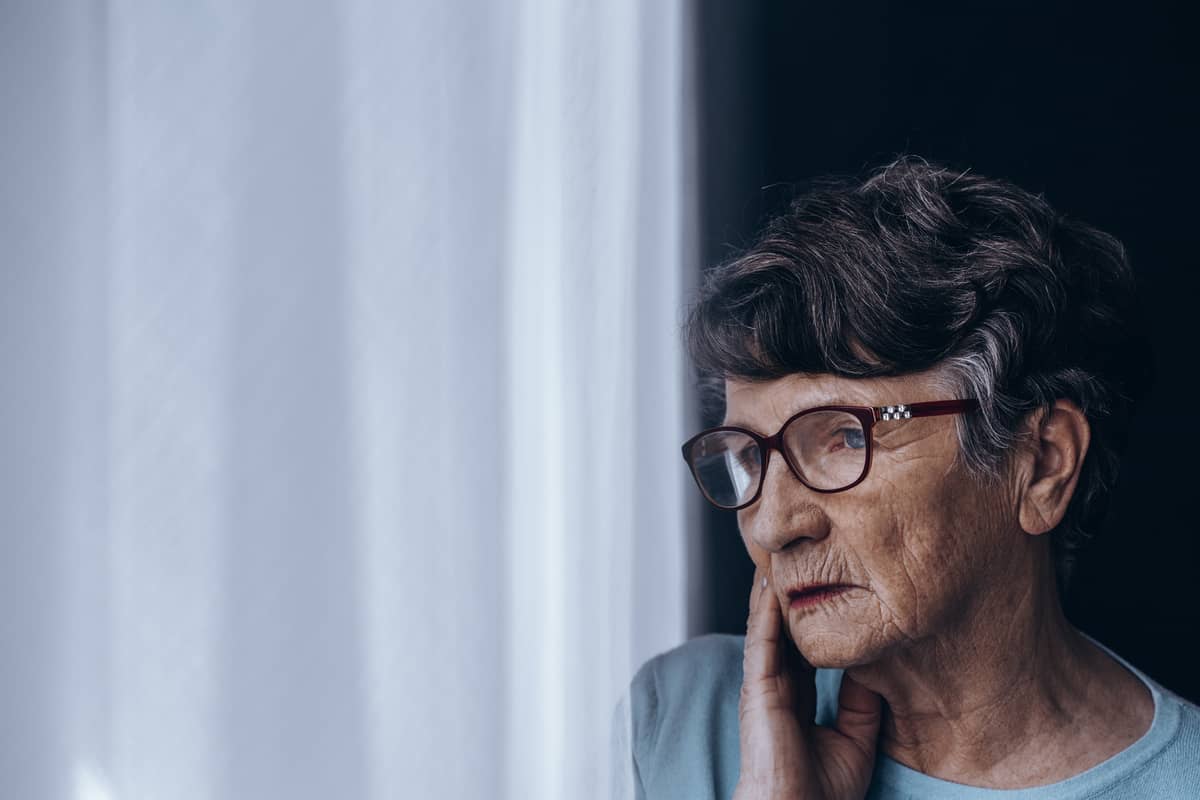 A senior woman looks out a window looking confused