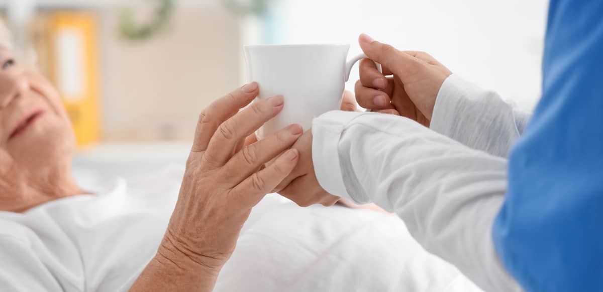 A caregiver giving a senior a cup
