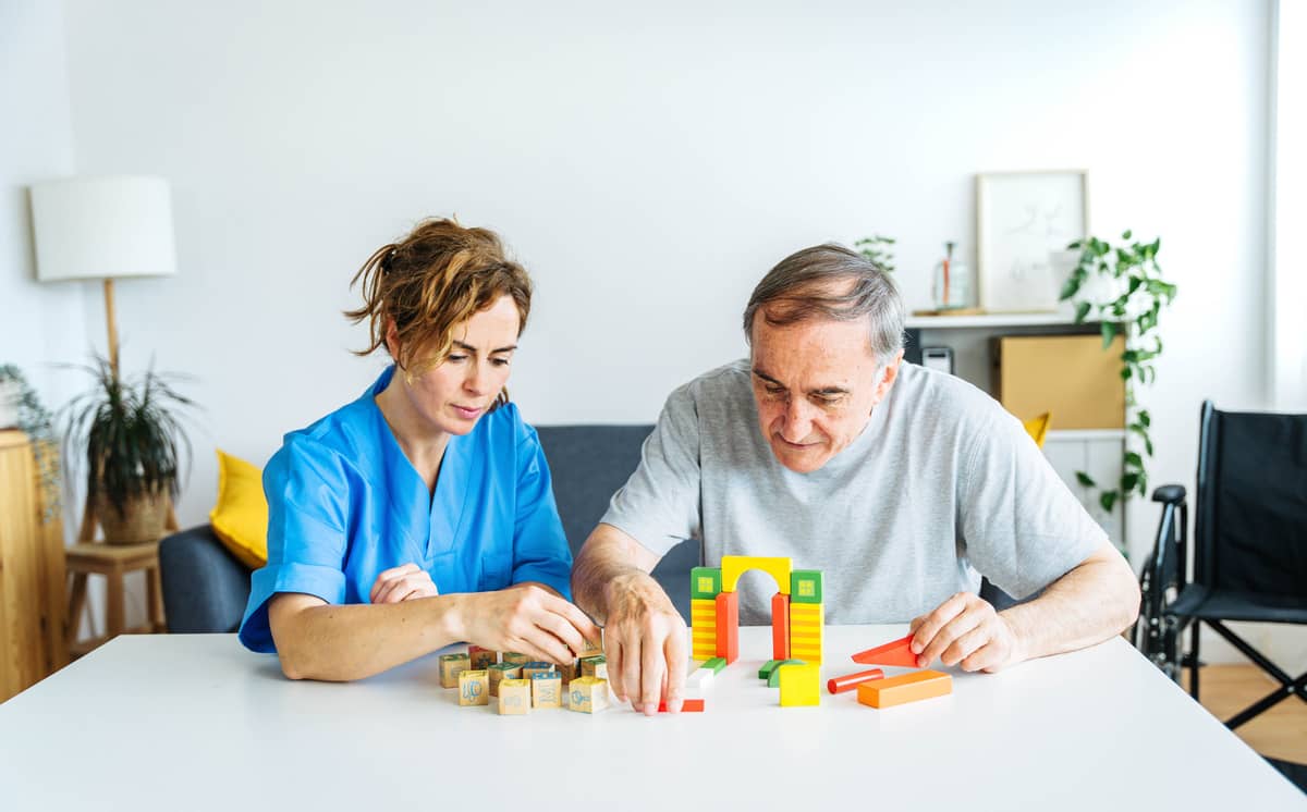 A female caregiver helping a senior man with a puzzle