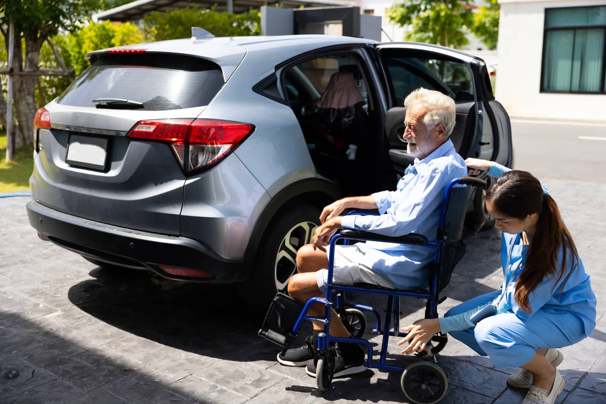 A home care provider helping a senior man in a wheelchair get in a car