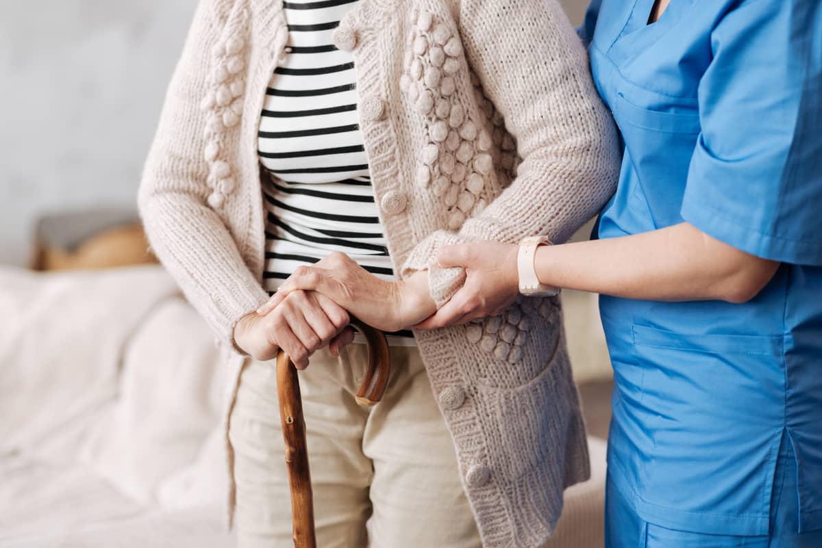 A caregiver helping a senior with a cane