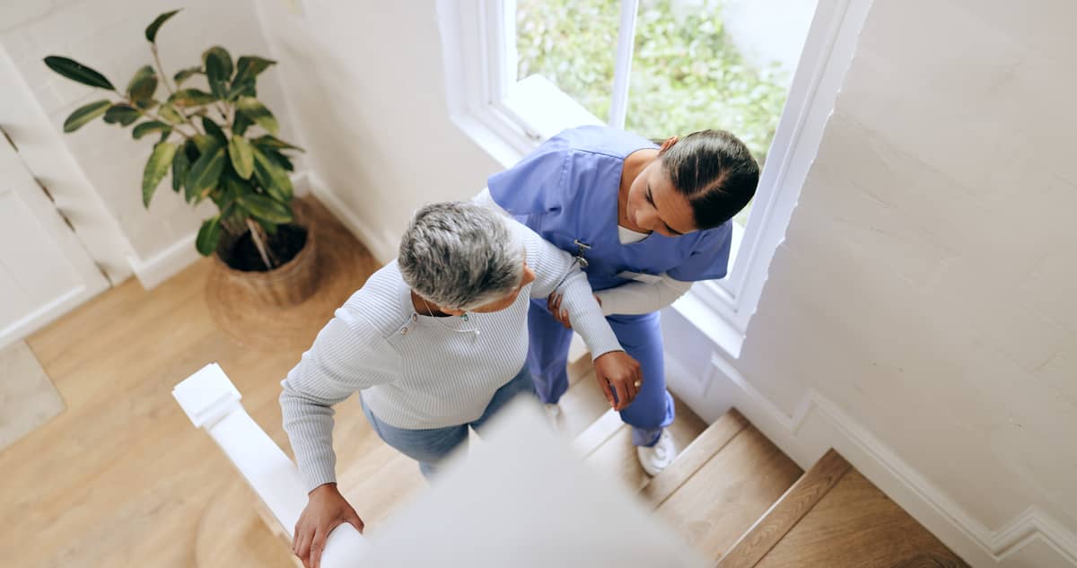 A home care provider helping a senior woman up the stairs