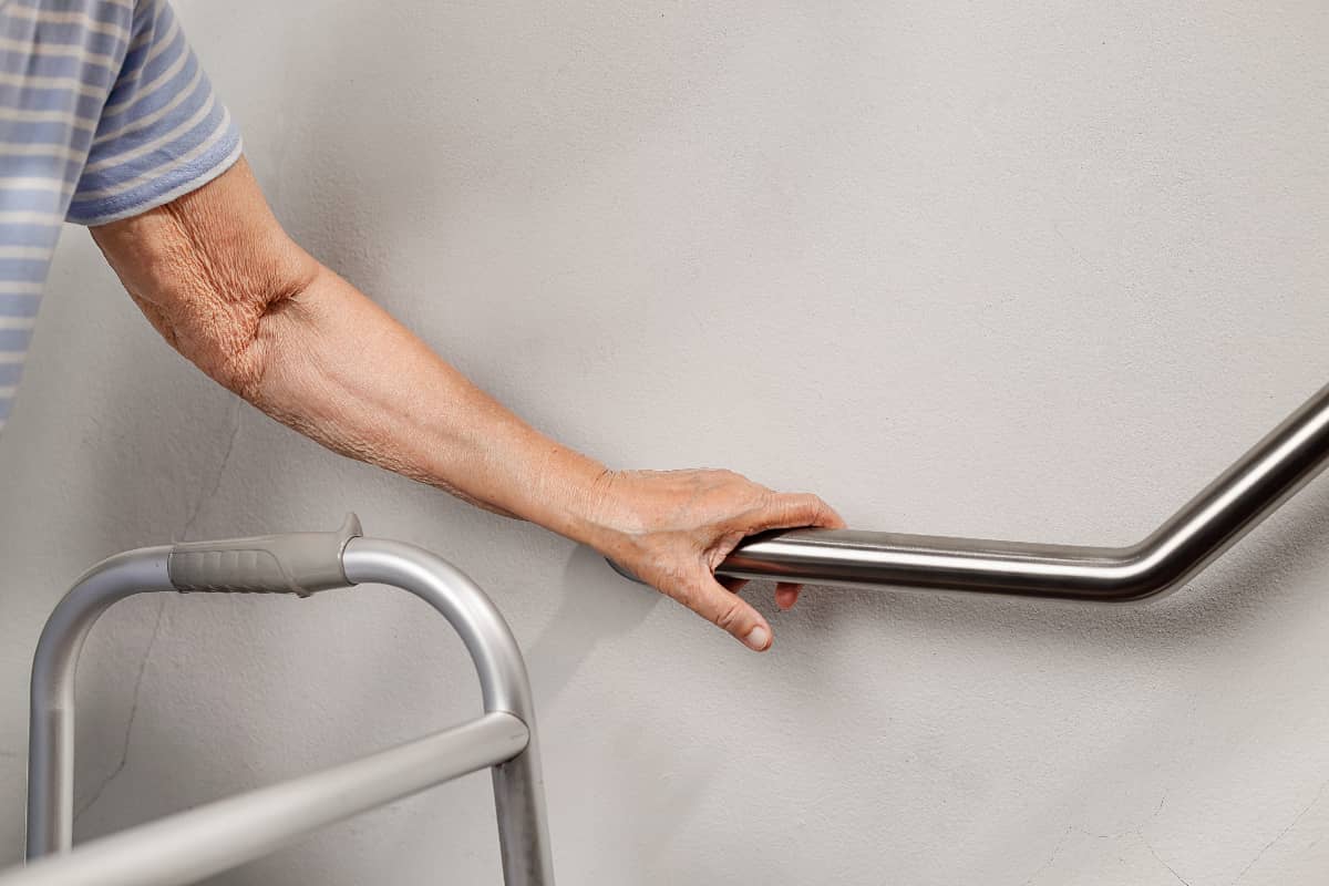 A senior with a walker grabbing a hand rail