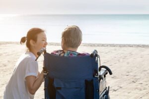 Woman in wheelchair with a caregiver by the beach
