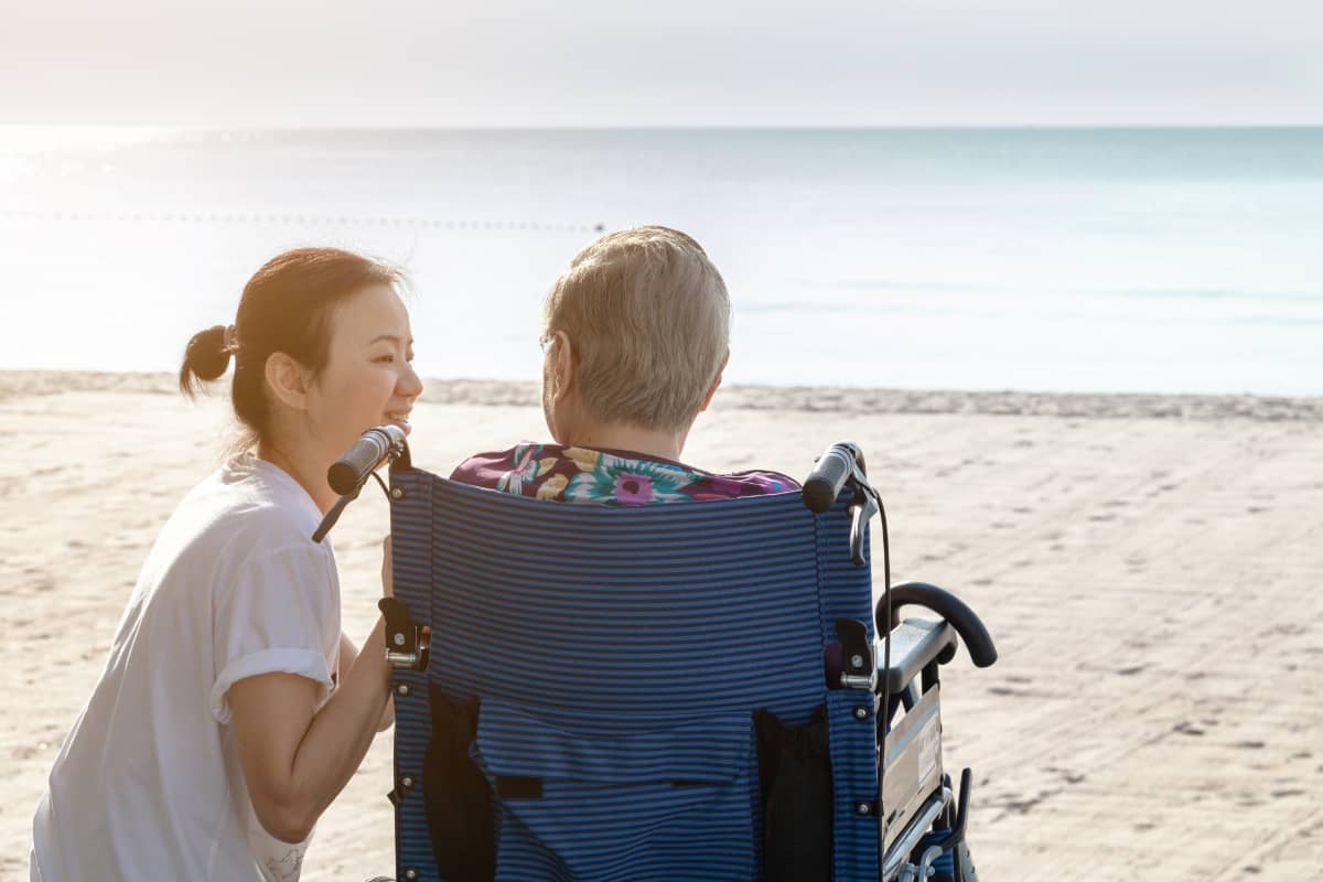 Woman in wheelchair with a caregiver by the beach