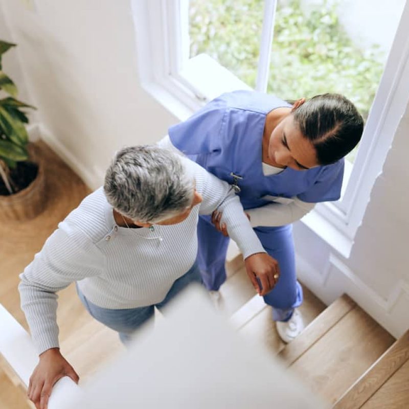 A home care provider helping a senior woman up the stairs